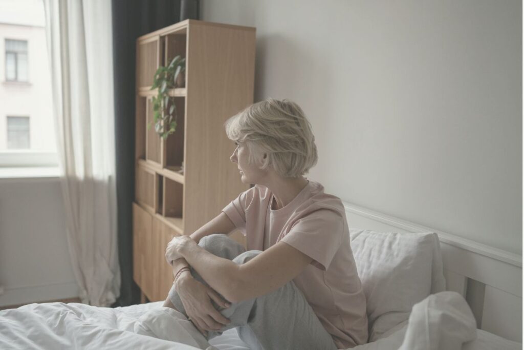 Frau sitzt wach im Bett und denkt nach als Symbol warum dein Kopf nicht zur Ruhe kommt
