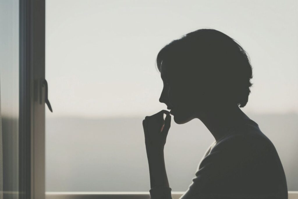 Silhouette einer nachdenklichen Frau am Fenster als Symbol dafür, wenn alles zuviel wird.