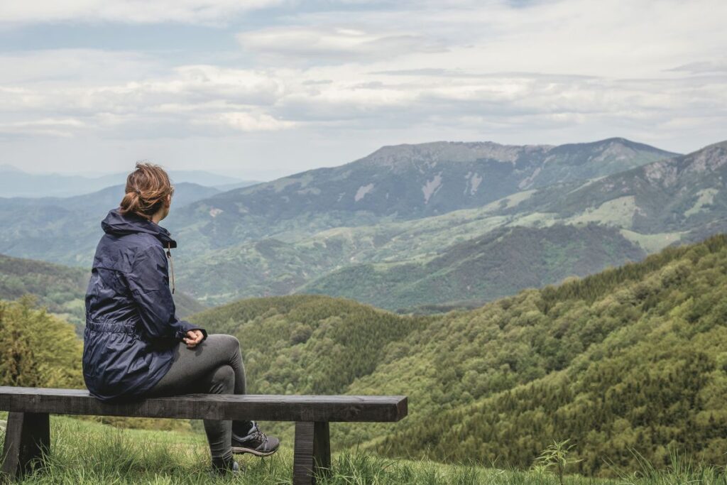 Eine Frau sitzt nachdenklich auf einer Bank mit Bergpanorama blogbeitrag frau bank berge