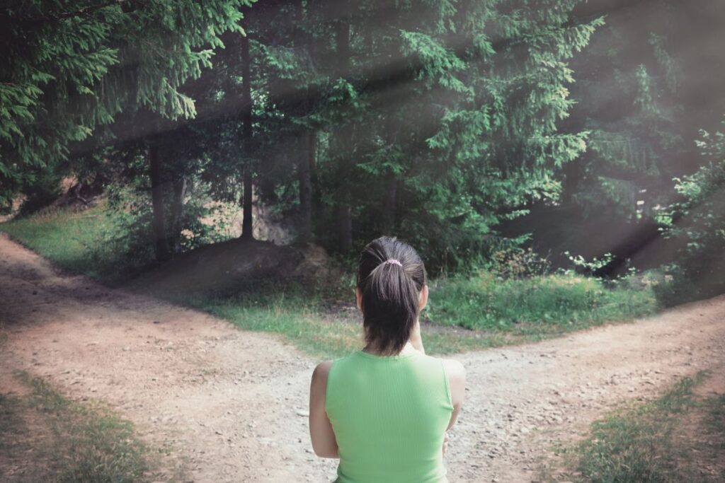 Frau steht nachdenklich an Weggabelung im Wald als Symbolbild für Angst vor falschen Entscheidungen verstehen.