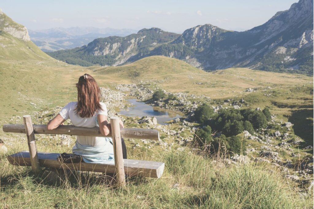 blogartikel 8 2 Eine Frau sitzt auf einer bank mit Blick auf berge und ein ruhiges Tal.